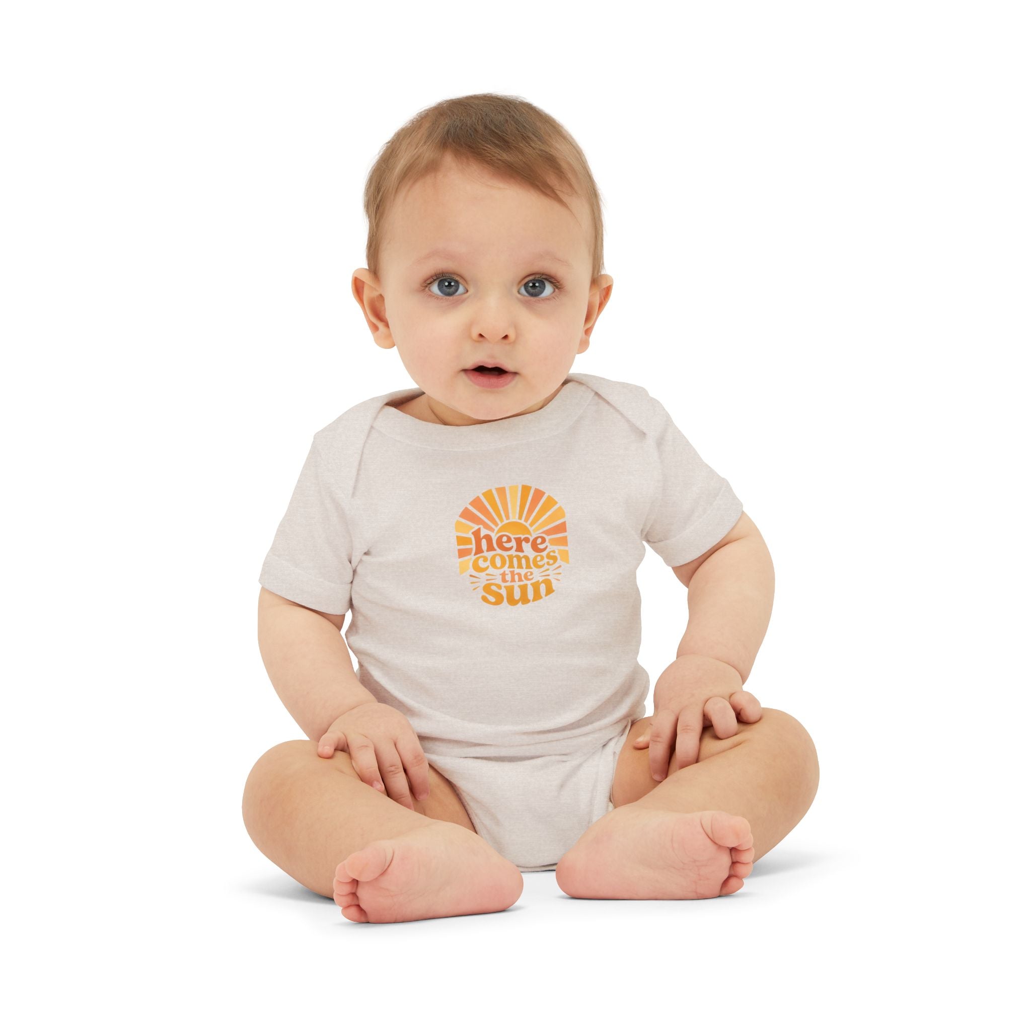 Cute Baby Bodysuit in light color with the phrase 'Here Comes The Sun' on infant model sitting down.
