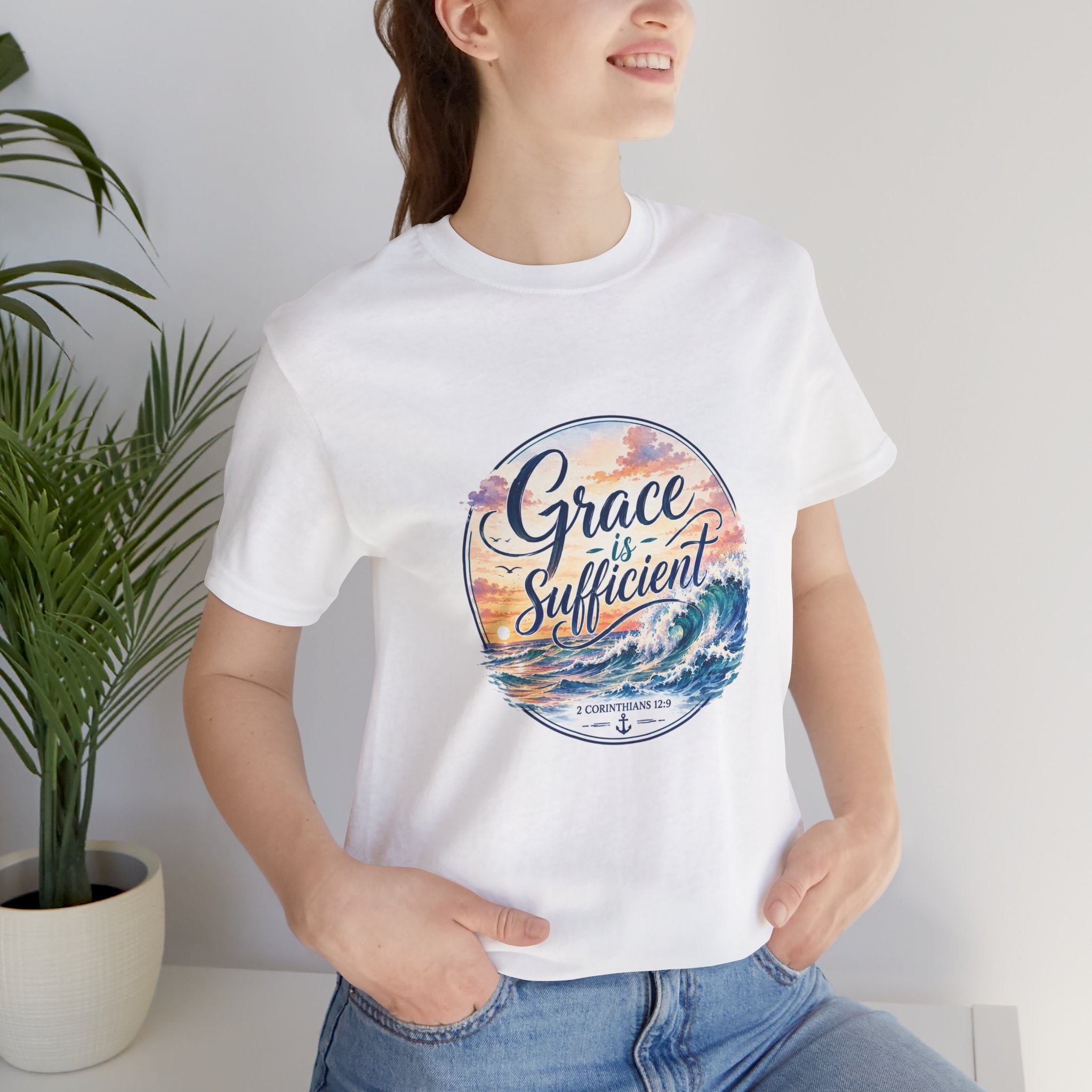 Model wearing Grace Is Sufficient Tee featuring a seaside graphic design with pastel sunset and ocean wave details.