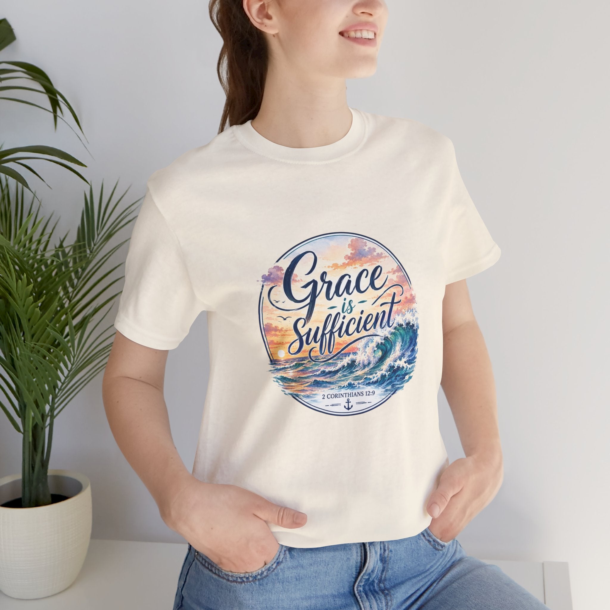 Grace Is Sufficient Tee worn by a smiling woman, featuring a pastel sunset design with ocean waves.