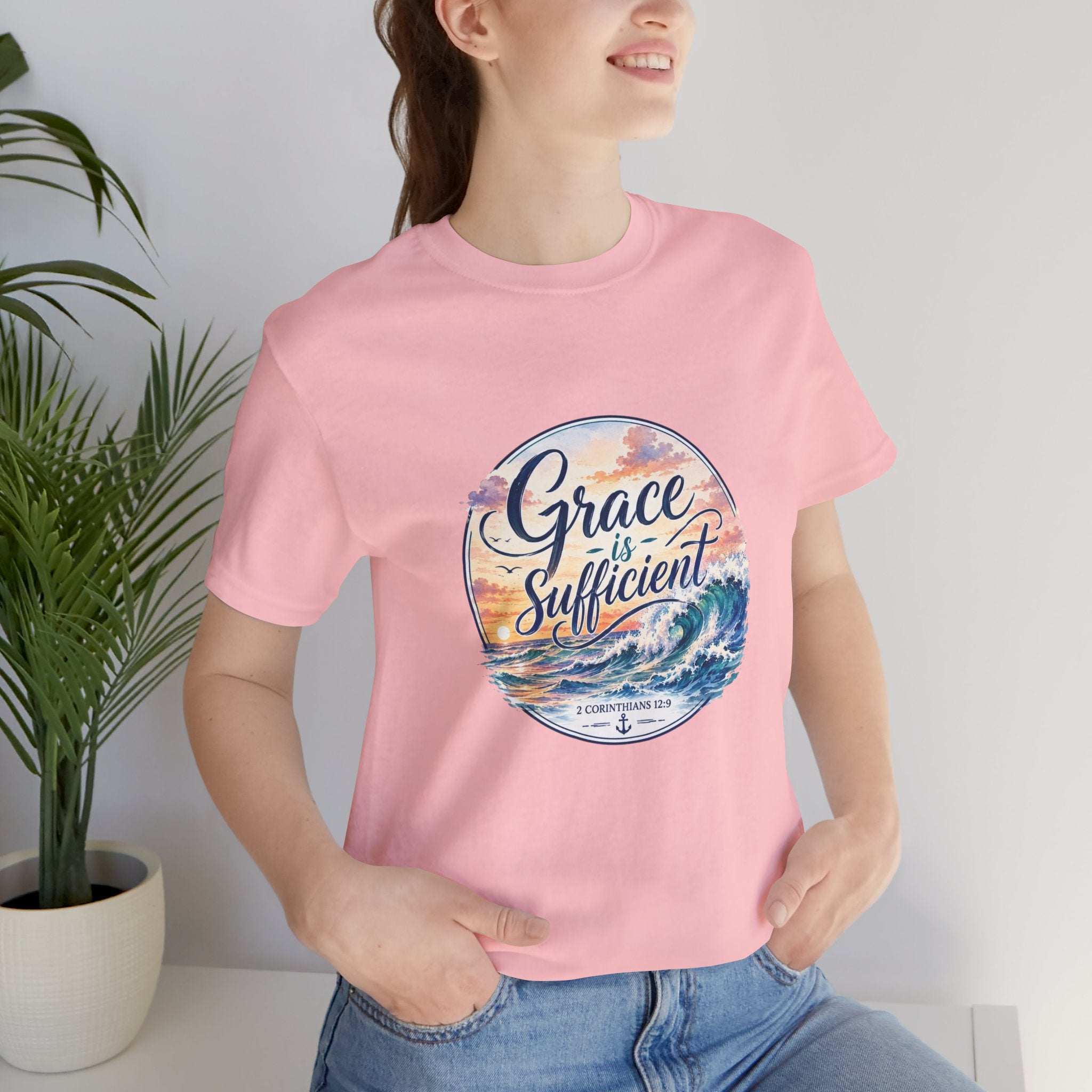 Grace Is Sufficient Tee worn by model, featuring ocean graphic and pastel sunset design on soft pink cotton.